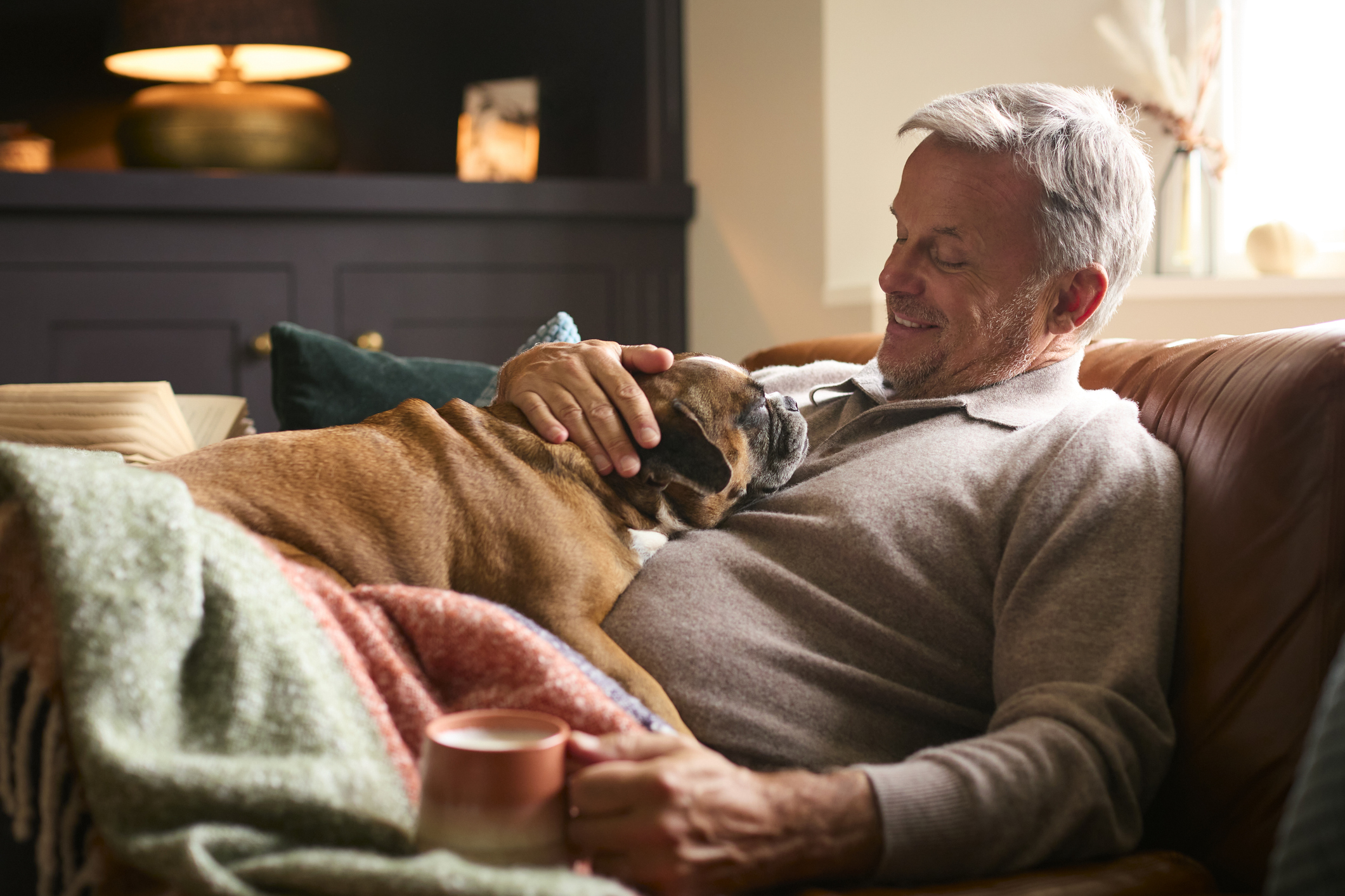 Un homme souriant caresse son chien allongé sur lui dans le canapé.