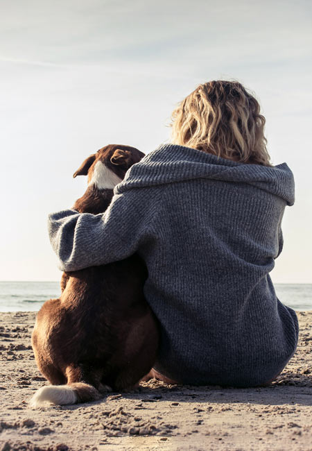 Une femme et un chien enlacés regardent la mer
